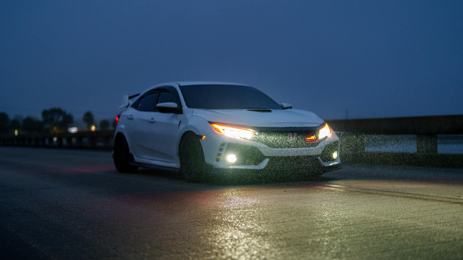 Białe sportowe auto jedzie nocą w deszczu z włączonymi światłami
