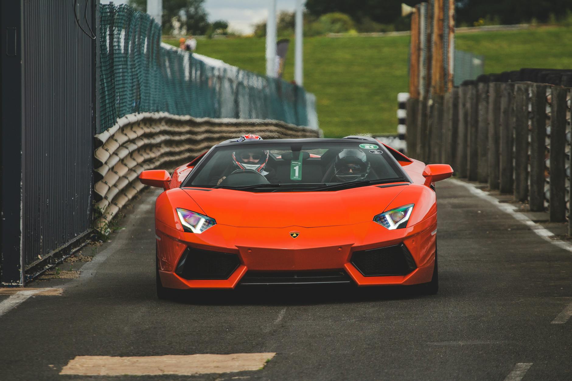 Pomarańczowe Lamborghini pędzi po zamkniętym torze z kierowcą w kasku
