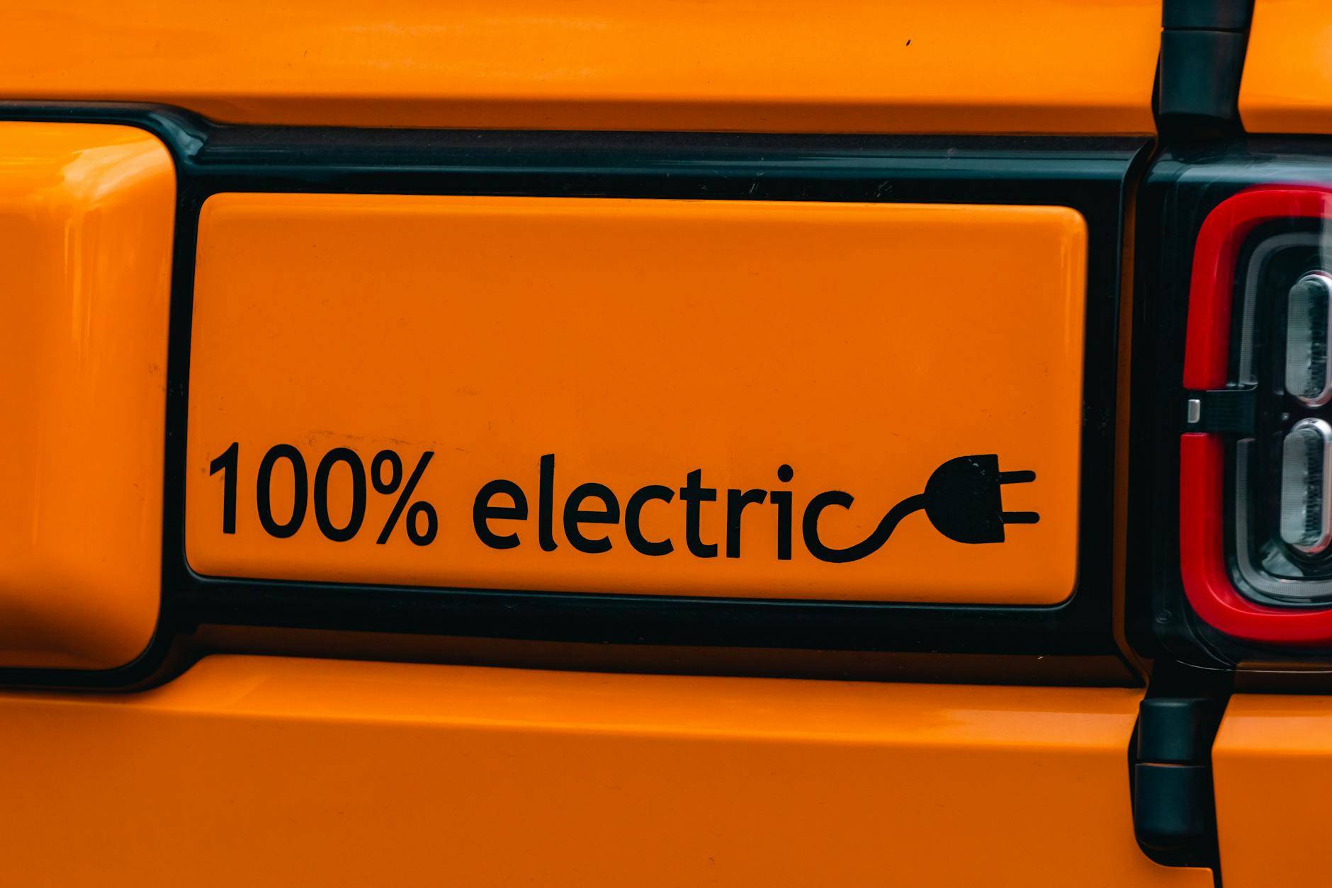 Pomarańczowy elektryczny samochód z napisem 100% electric
