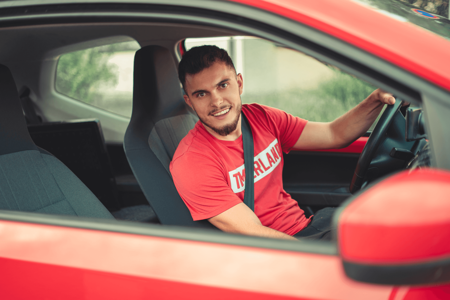 Młody mężczyzna prowadzi czerwoną Hondę w pasach bezpieczeństwa