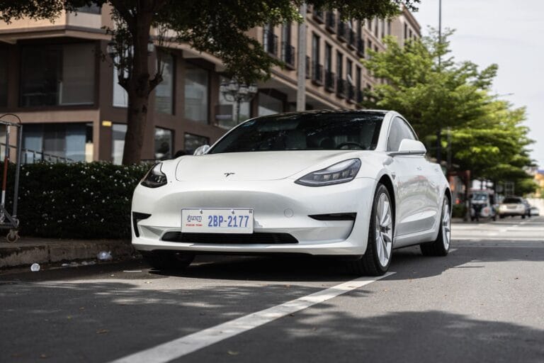 Biała Tesla Model 3 zaparkowana na miejskiej ulicy pod drzew